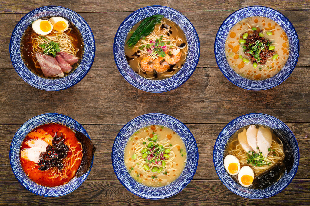 Set of different types of Japanese ramen, tantanmen, shio ramen, shrimp, wood mushrooms, top view on a wooden background, in blue traditional bowls