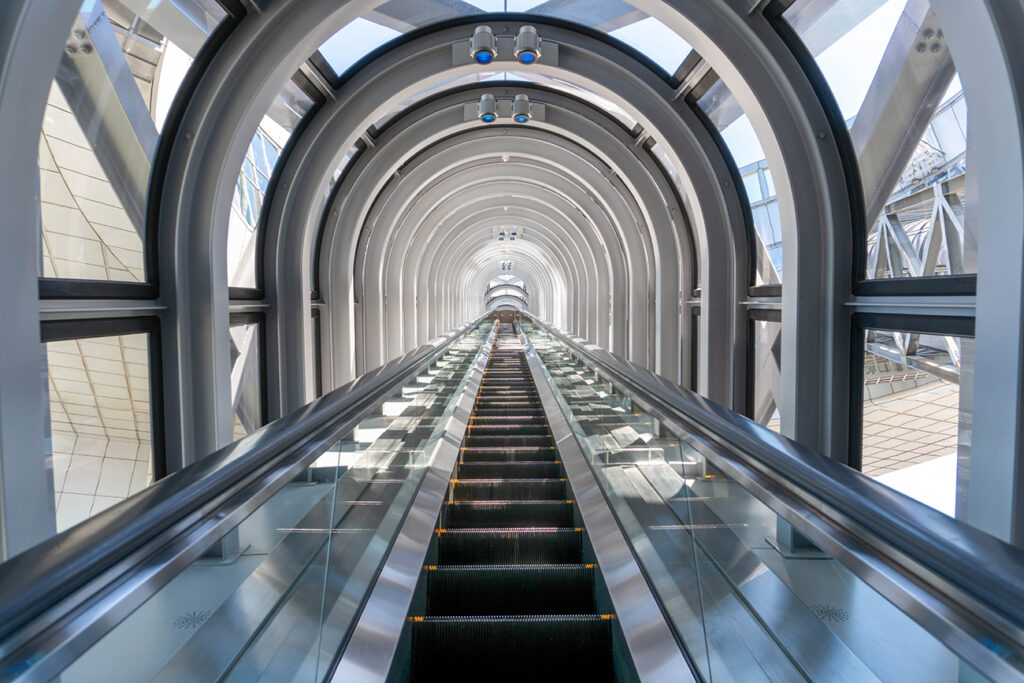 View from the bottom of a single upwards moving escalator surrounded by steel and glass arches