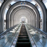 View from the bottom of a single upwards moving escalator surrounded by steel and glass arches